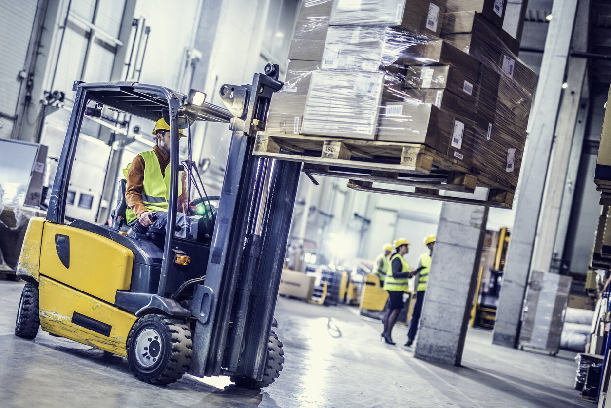 Supply chain worker moving wooden pallets with a forklift in a warehouse
