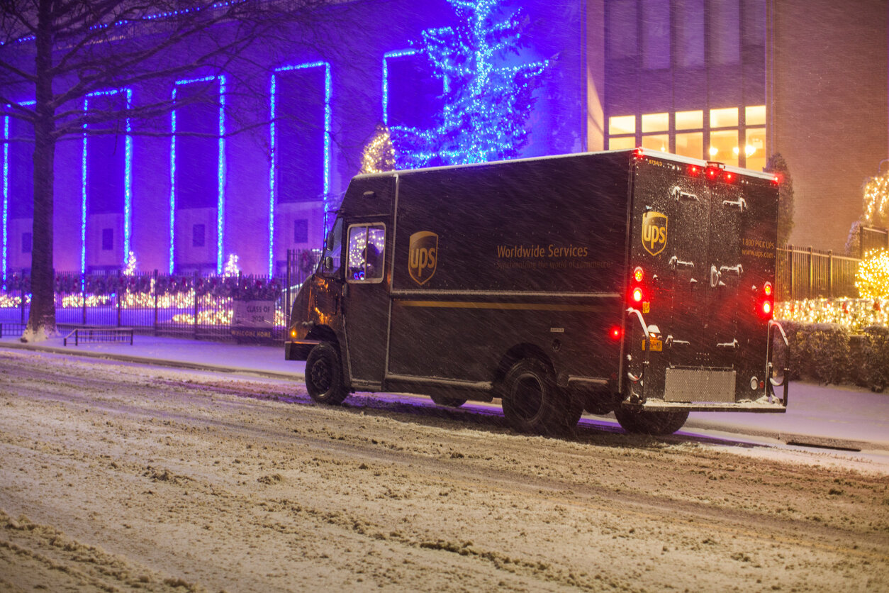 UPS delivery truck delivering holiday packages in a blizzard with holiday decorations in the background. Logistics and holiday shipping surcharges concept