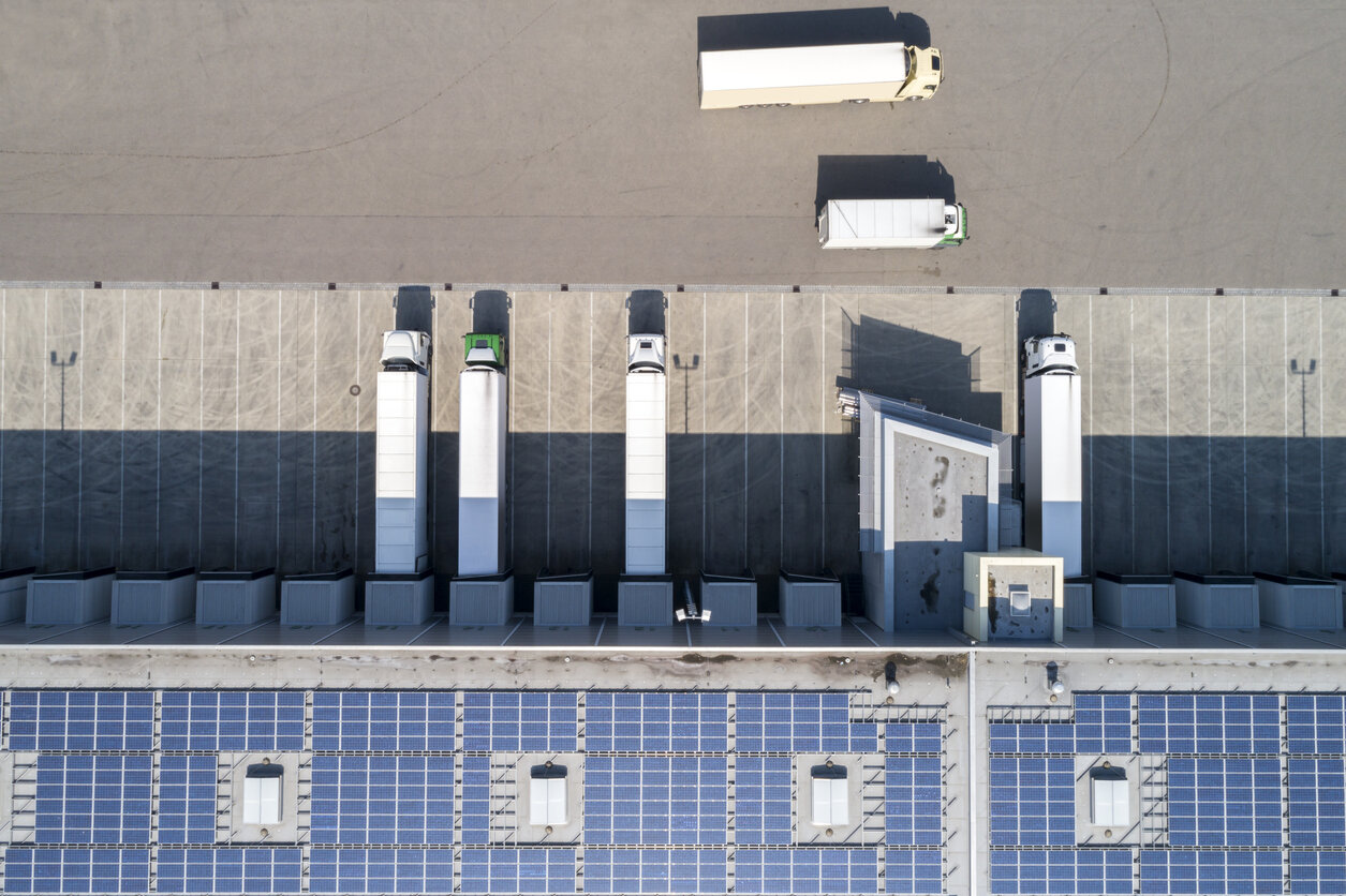 Aerial view of semi trucks cross docking at a large storehouse with solar panels on the rooftop encouraging eco-friendly supply chain.