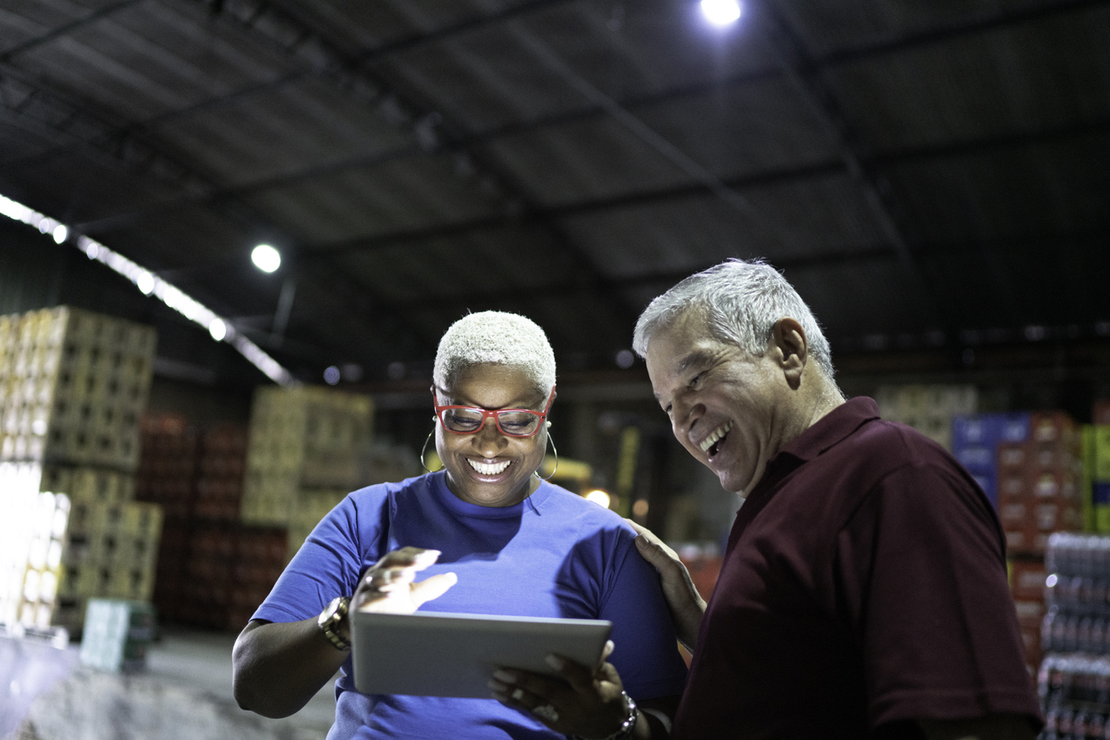 Two happy people celebrating a 3PL partnership with a dedicated fulfillment partner. Woman is holding a tablet and male worker is smiling in a warehouse.