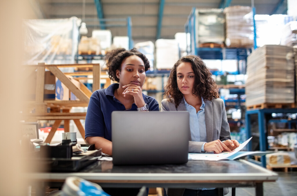Supply chain management inventory management: Female worker with supervisor working on laptop. Factory workers working together.