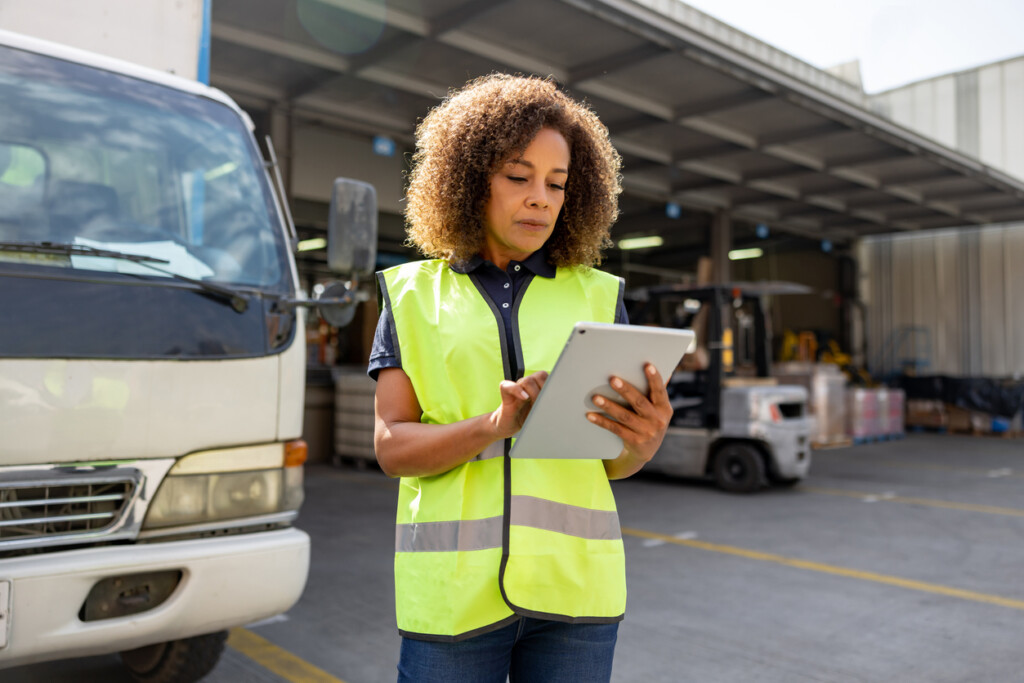 Woman supervising the dispatch of trucks at a distribution warehouse with a digital tablet. Delivery and transportation logistics solutions