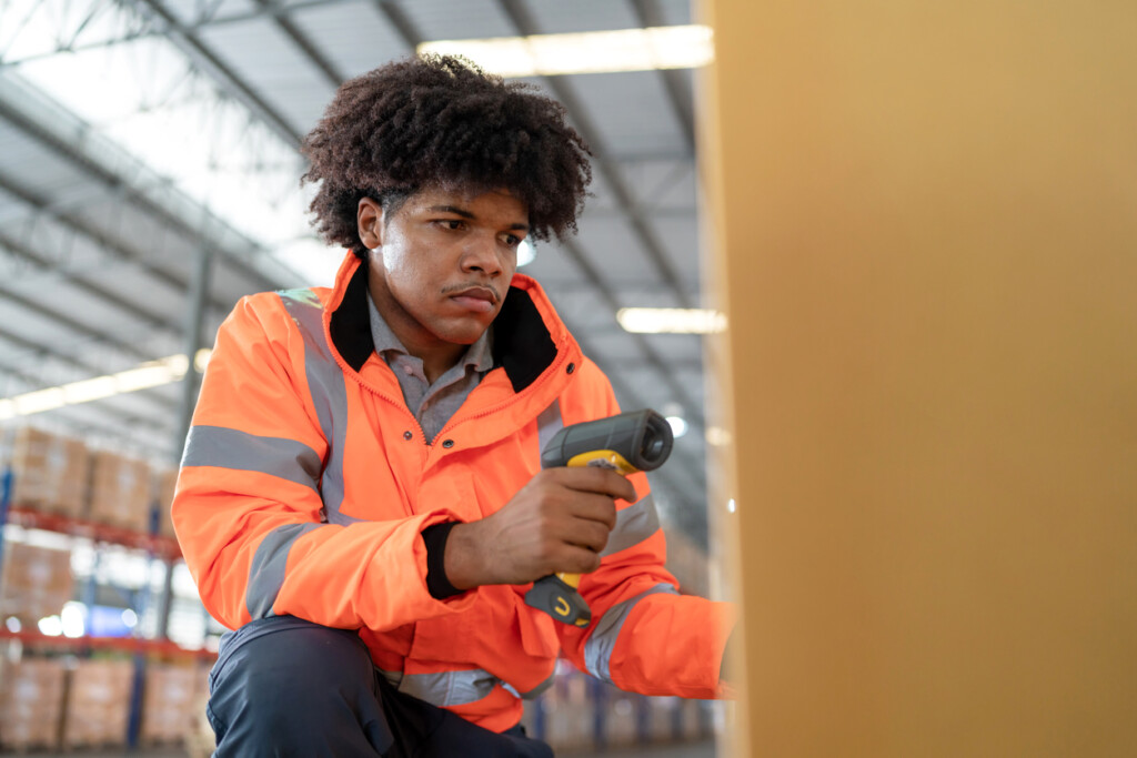 Warehouse worker in reflective safety suit using handheld barcode reader scan tag code on the parcel in the modern distribution warehouse. Recording stock data forreal-time inventory management.