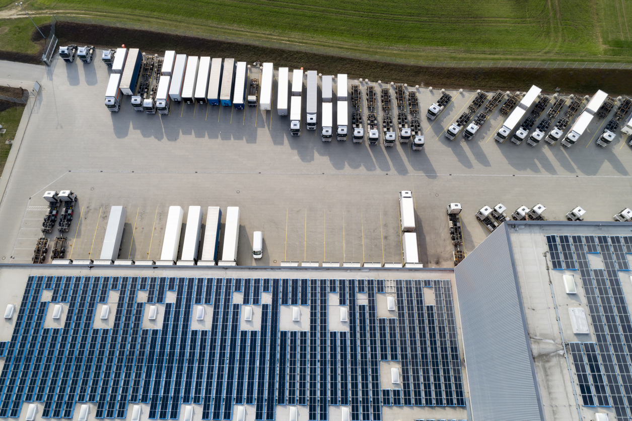 Aerial view of semi trucks unloading at a large storehouse with rooftop solar panels, highlighting sustainable logistics and supply chain operations.