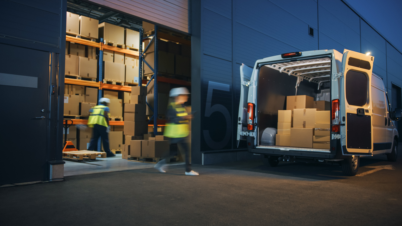 Creating Hybrid Retail Logistics Systems: Diverse team of workers loading a delivery truck with cardboard boxes outside a logistics distribution warehouse, demonstrating the integration of online orders and physical retail store stock in the supply chain.
