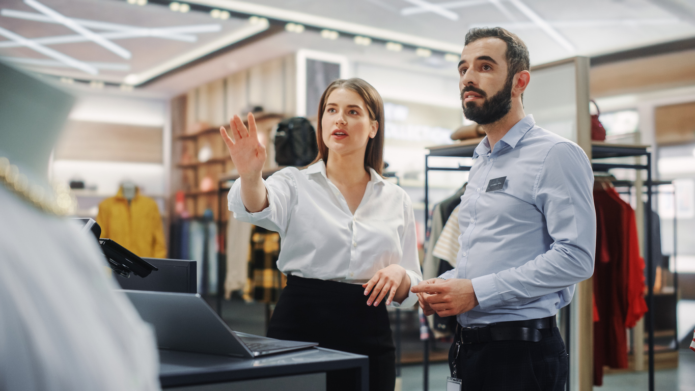 Retailer Logistics Challenges: Businesswoman and man discussing products in a clothing store, highlighting the complexities of inventory management and decision-making in physical retail.