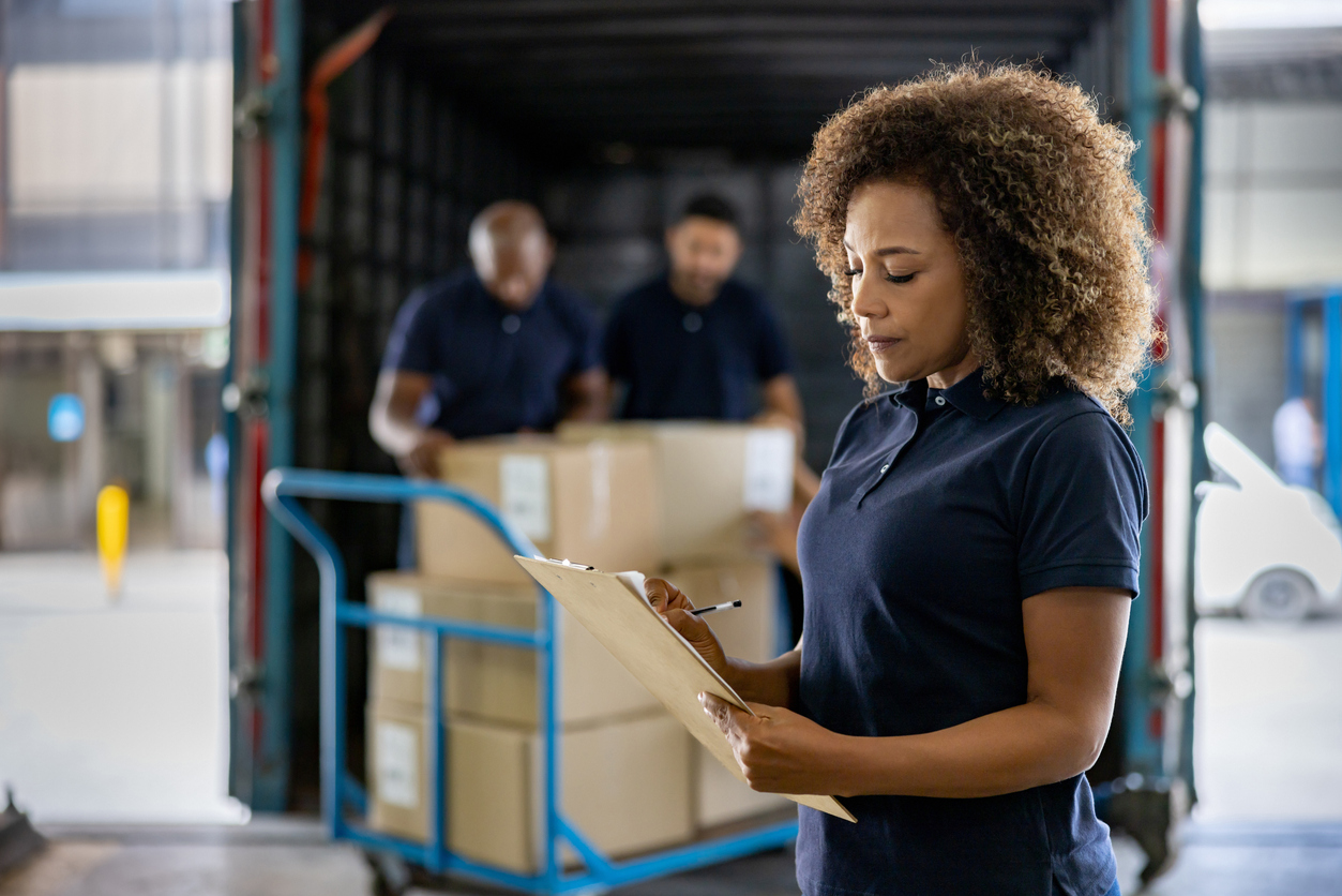 A woman in a supervisory role overseeing the shipping of cargo at a distribution warehouse. This image reflects the importance of monitoring retail chargebacks in supply chain account management.