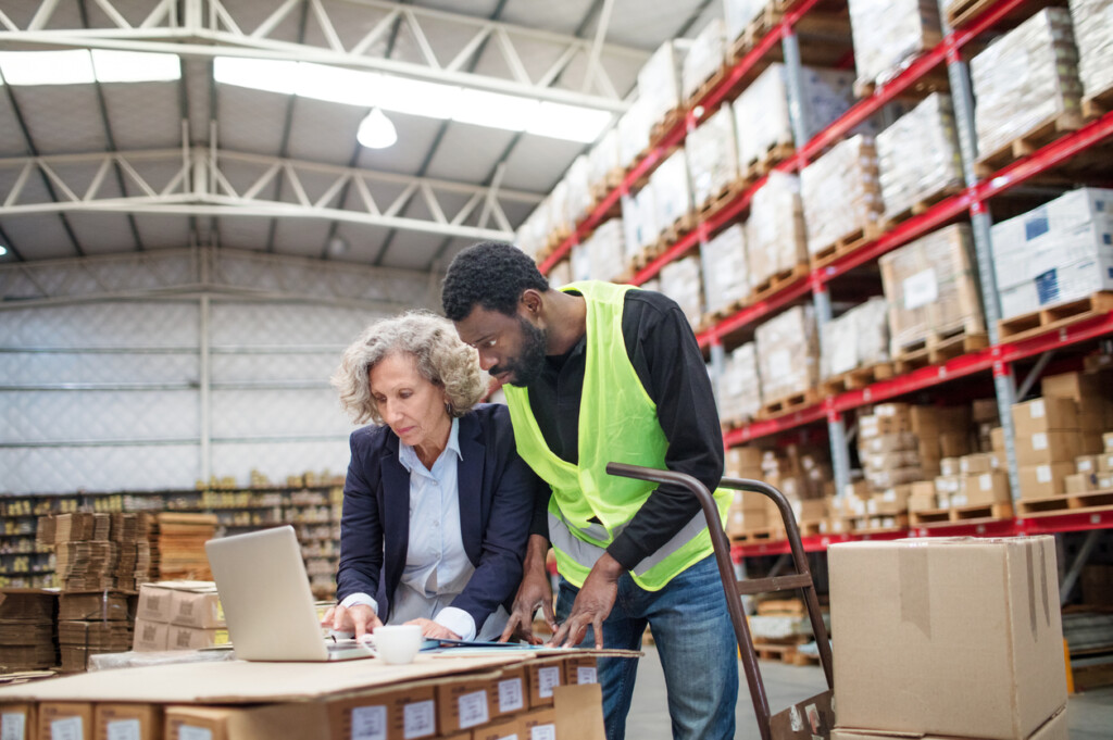 Third-party logistics (3PL) provider in a warehouse operations on a laptop, in collaboration with a worker. Emphasizing partnership and technology for enhanced supply chain efficiency