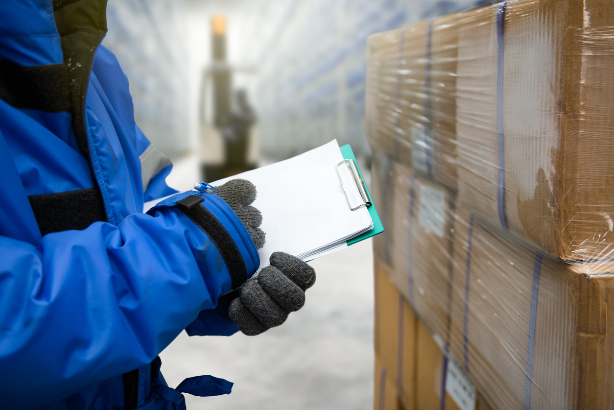 Closeup shooting hand of worker with clipboard checking goods in freezing room or warehouse