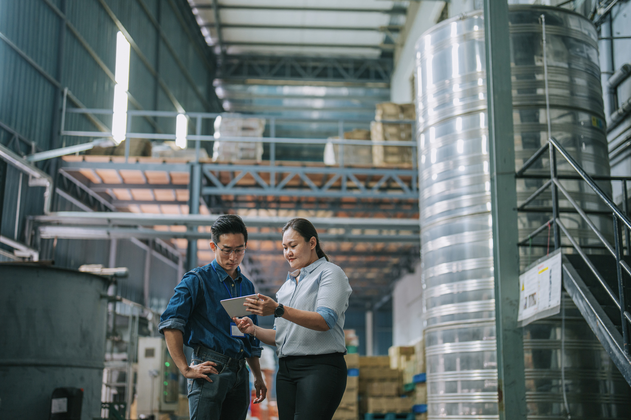 Warehouse manager discussing the SQF certification process on a tablet to a man in a food processing warehouse