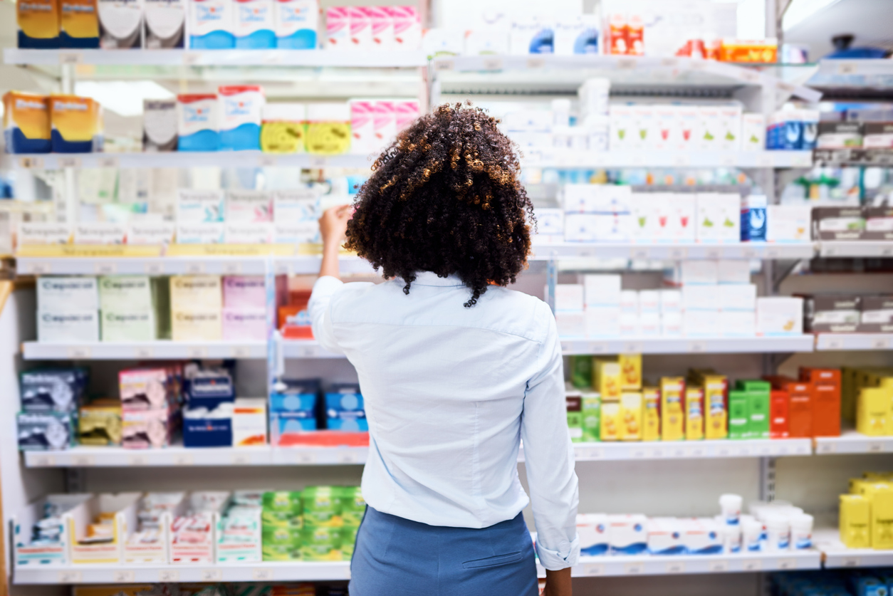 Rearview shot of a young woman looking at products in a store or pharmacy. The woman is in focus and the products are blurred. 