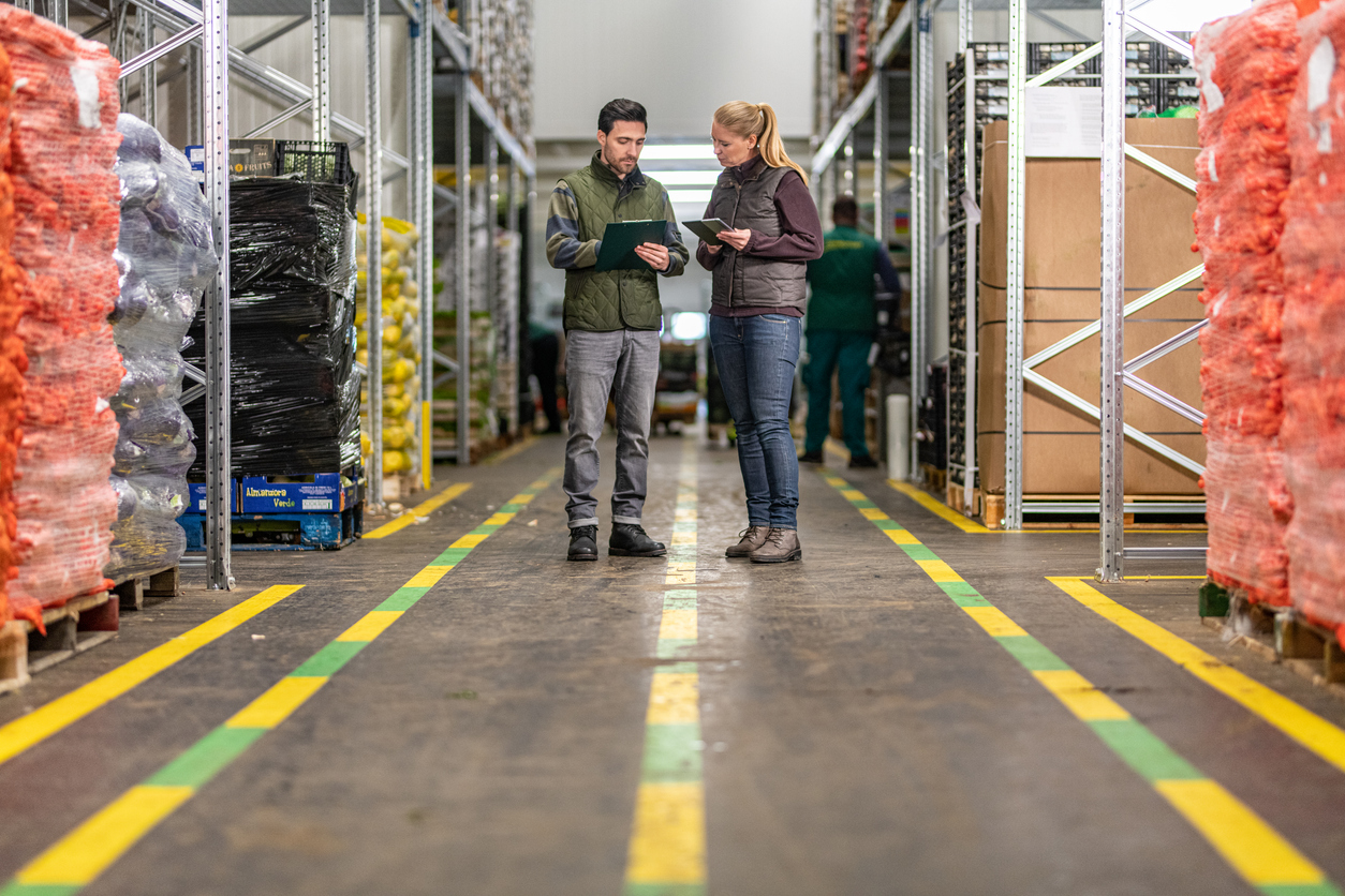 Two workers discussing SQF certification with a clipboard and digital tablet while maintaining compliance