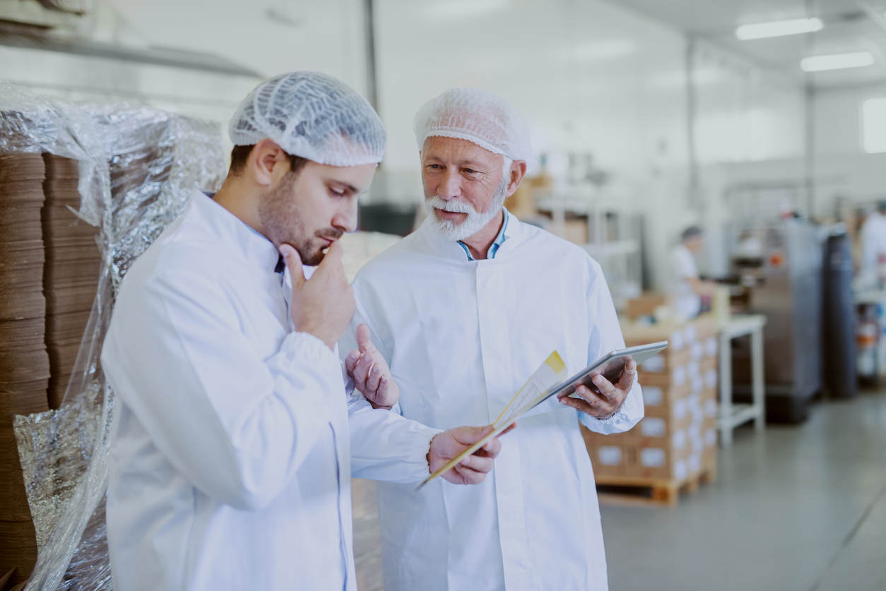 Quality control worker and USDA inspector in sterile white uniforms holding a tablet and talking about USDA certifications