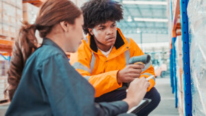 Serious warehouse workers crouching down and checking boxes on shelves with a scanner, highlighting product traceability and recall management.