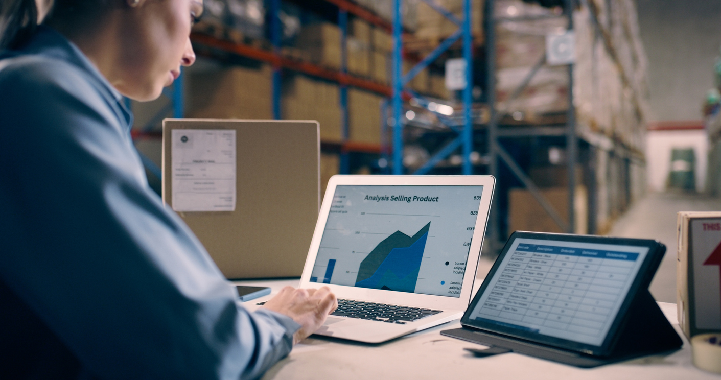 Warehouse employee analyzing e-commerce data on a laptop in a modern warehouse, highlighting the use of WMS for efficient inventory management and retailer compliance