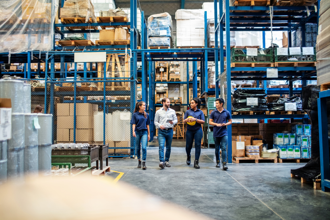 Warehouse employees working for a 3PL company walking through an aisle and discussing logistics operations, surrounded by tall shelves filled with inventory.