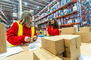 Two women working together organizing shipments in a distribution warehouse, illustrating the kitting process for streamlined order fulfillment and logistics
