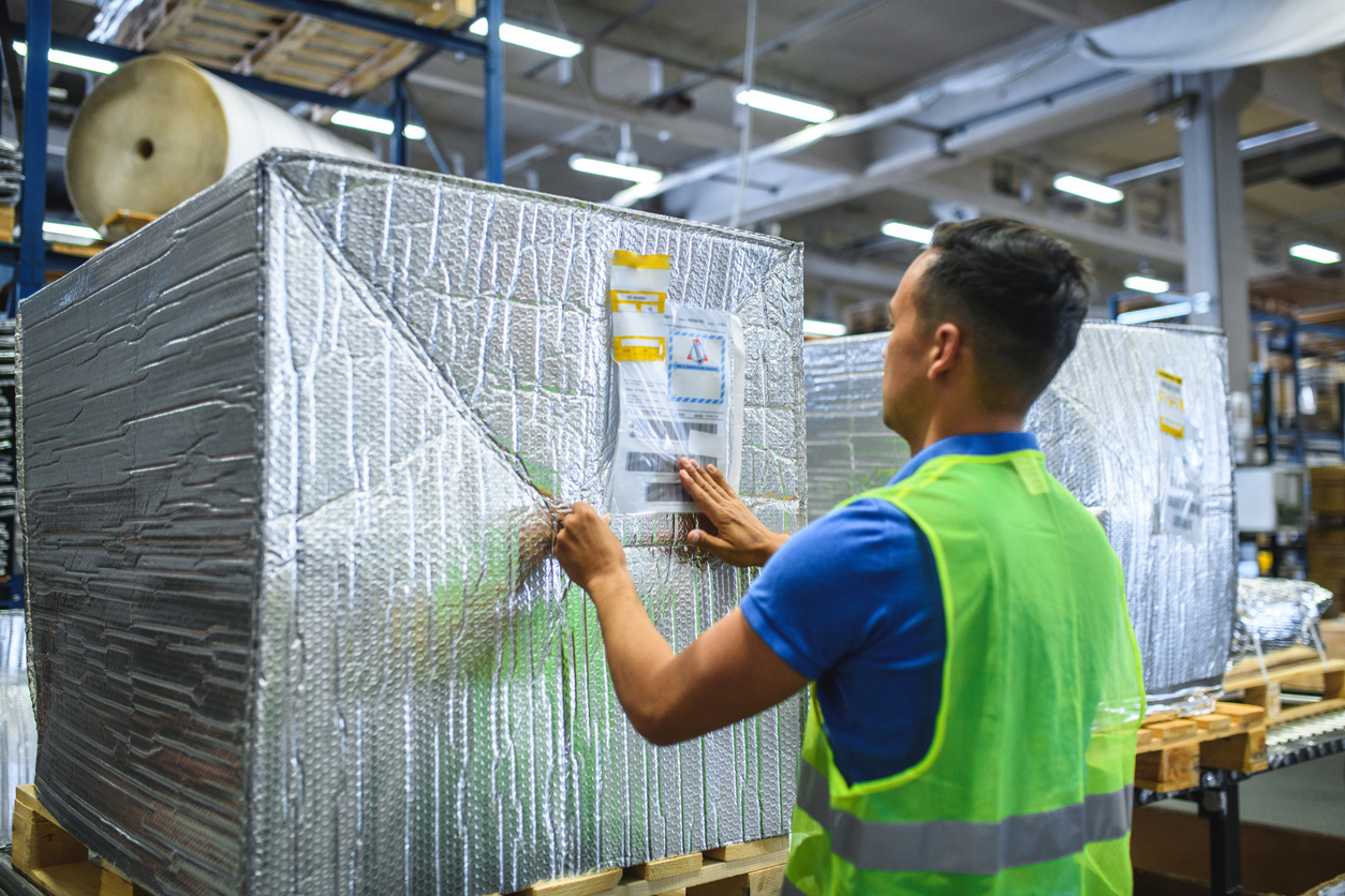A worker in a green reflective vest handling uniquely packaged boxes in a warehouse, representing customized logistics solutions in fulfillment partnerships.