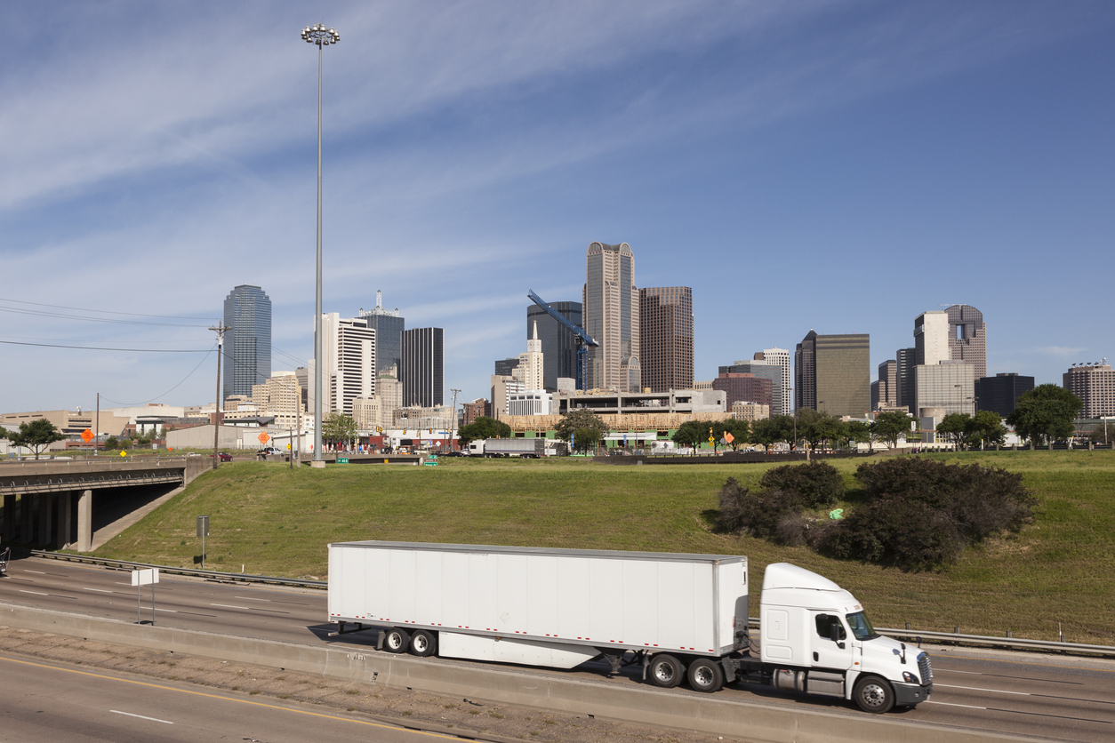 Truck on the highway with Dallas downtown skyline in the background. Texas, United States. Showcasing infrastructure that supports fast fulfillment center operations in Houston.