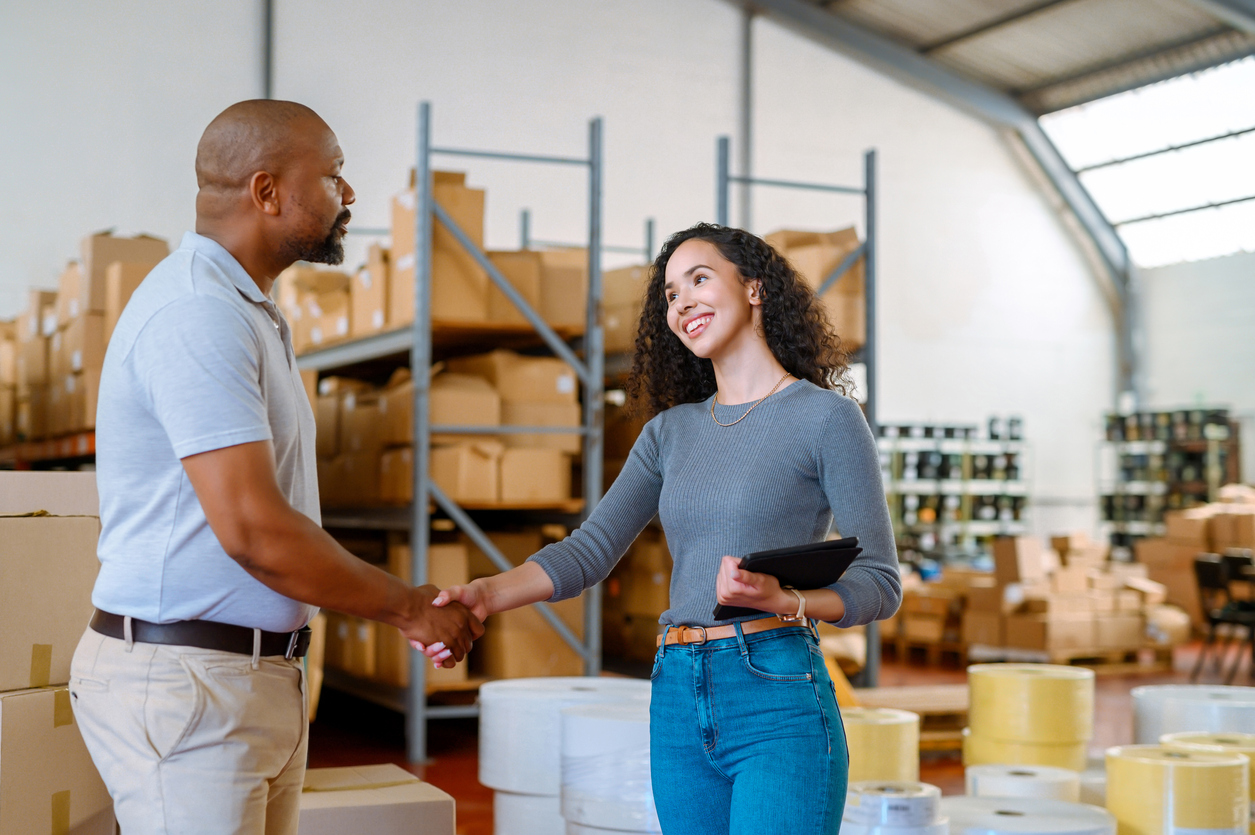 Logistics team and business owner shaking hands in a warehouse, symbolizing a strong subscription fulfillment partnership and operational success.