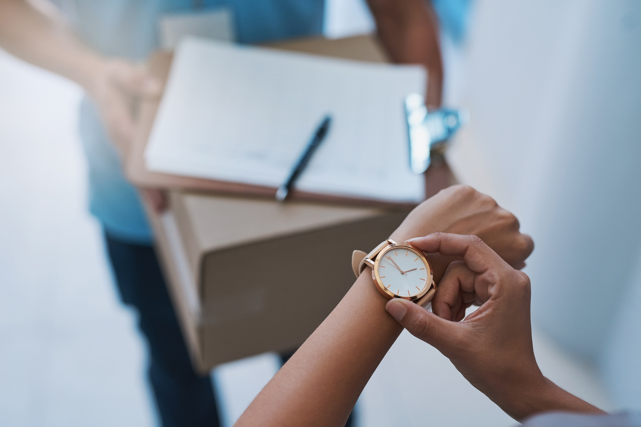 Woman checking the clock while receiving a delivery, reflecting customer frustration with delays tied to rising parcel costs