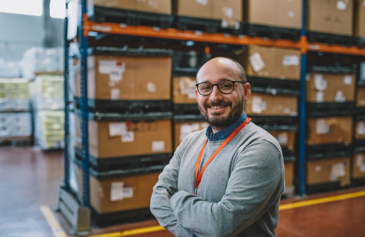 Smiling warehouse manager standing in a warehouse corridor, representing a reliable fulfillment partner in multichannel operations.