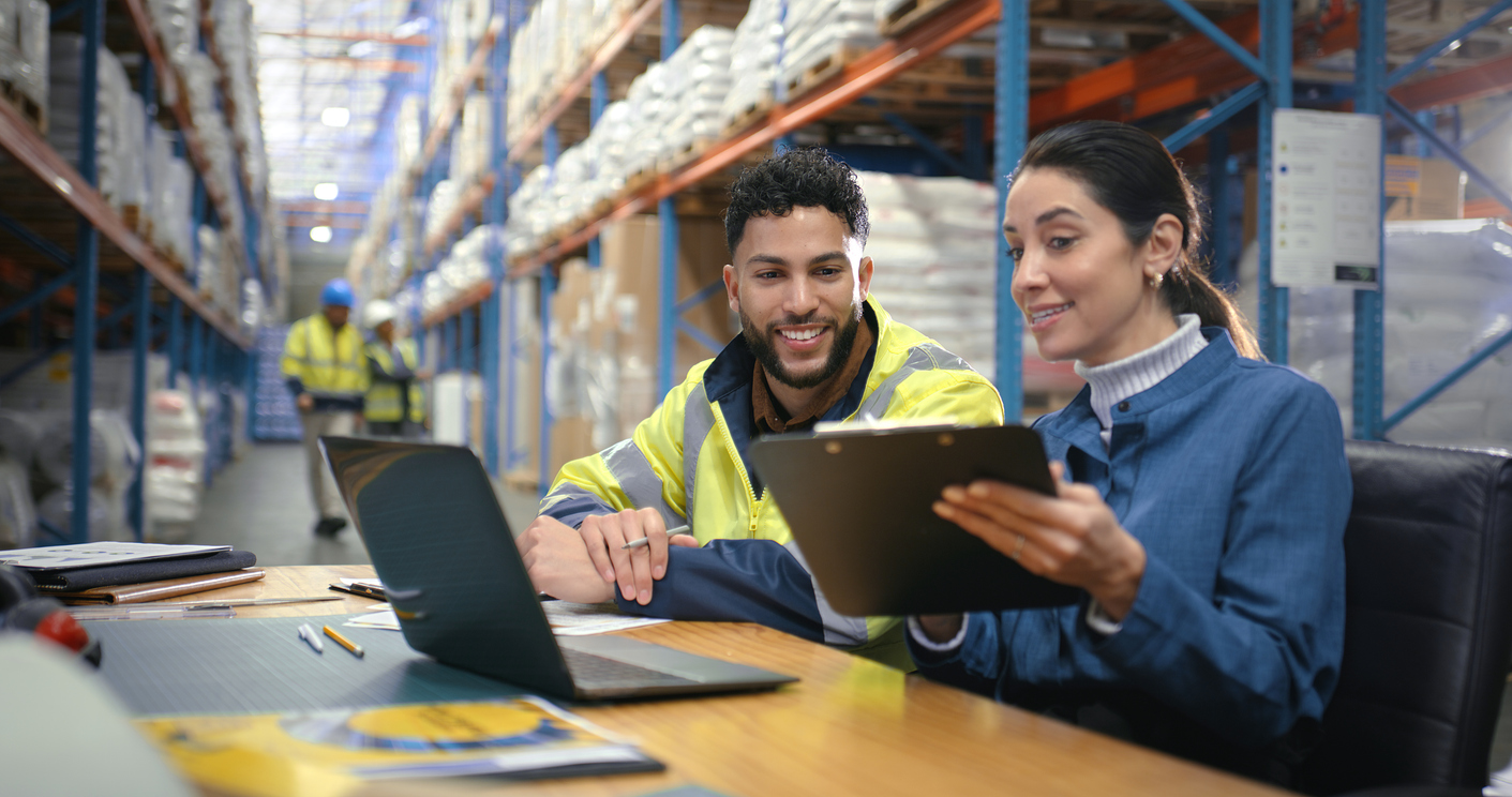 Team reviewing logistics strategy on a laptop in a distribution center, preparing for publisher fulfillment disruptions like the USPS BPM phase-out.