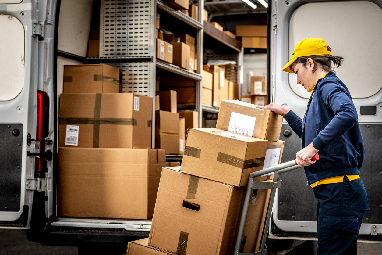 Smiling courier loading packages onto a hand truck in a warehouse, symbolizing efficient human involvement in D2C fulfillment.