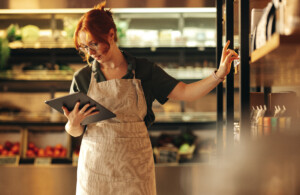 Female supermarket owner using a digital tablet while standing in her shop. Young female entrepreneur running her small business using wireless technology.