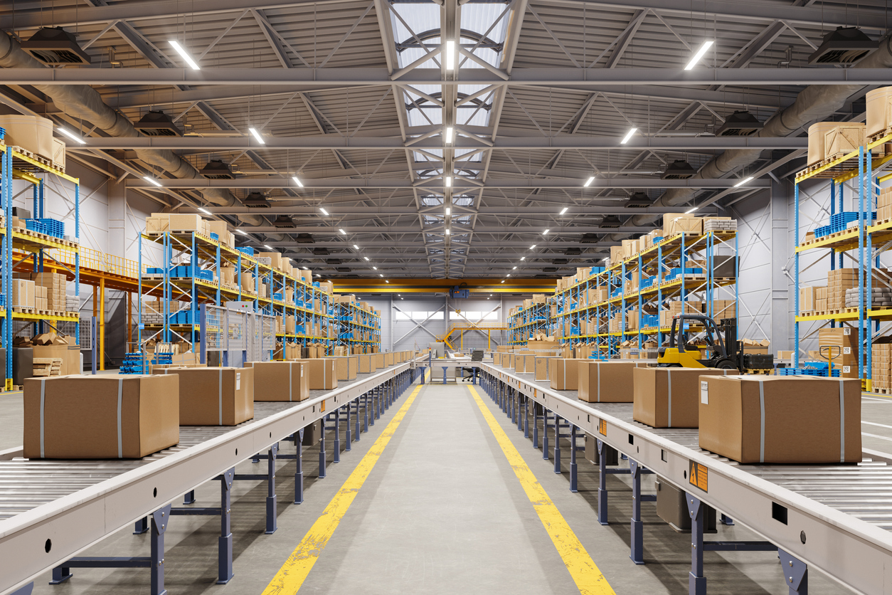 Cardboard boxes moving on a conveyor belt in a distribution warehouse, representing high-volume big-box fulfillment operations.