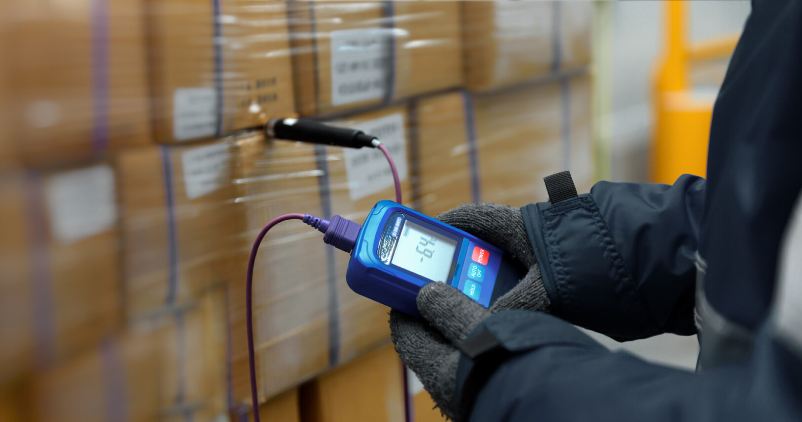 Warehouse worker checking pallet temperature with a handheld probe as part of temperature-controlled shipping procedures.