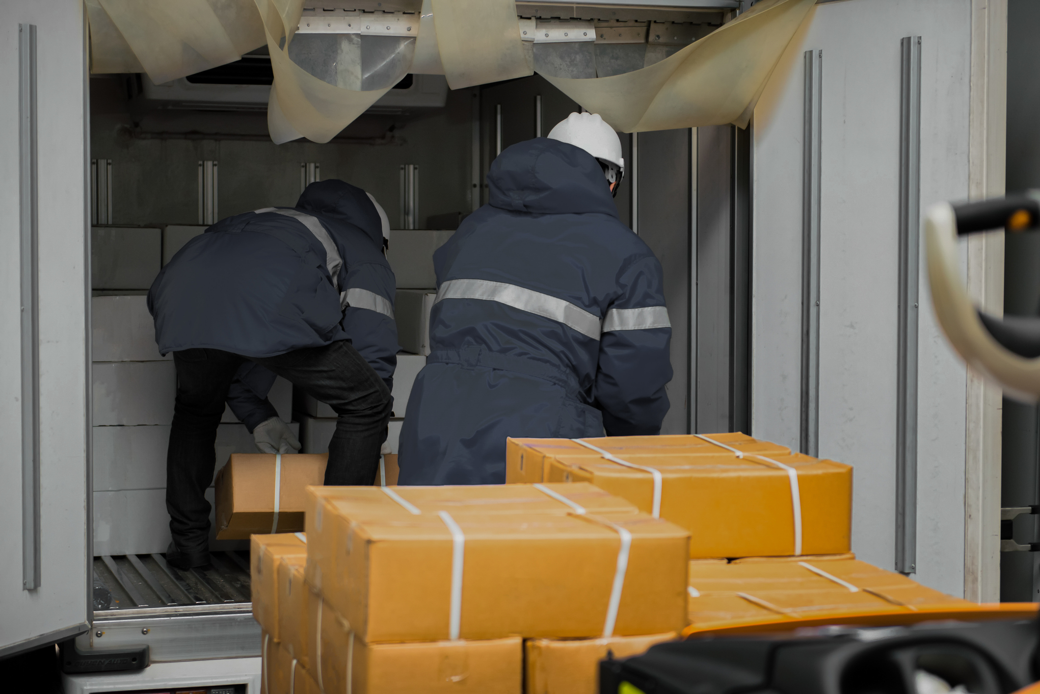 Workers loading boxes into a refrigerated truck during temperature-controlled shipping operations.
